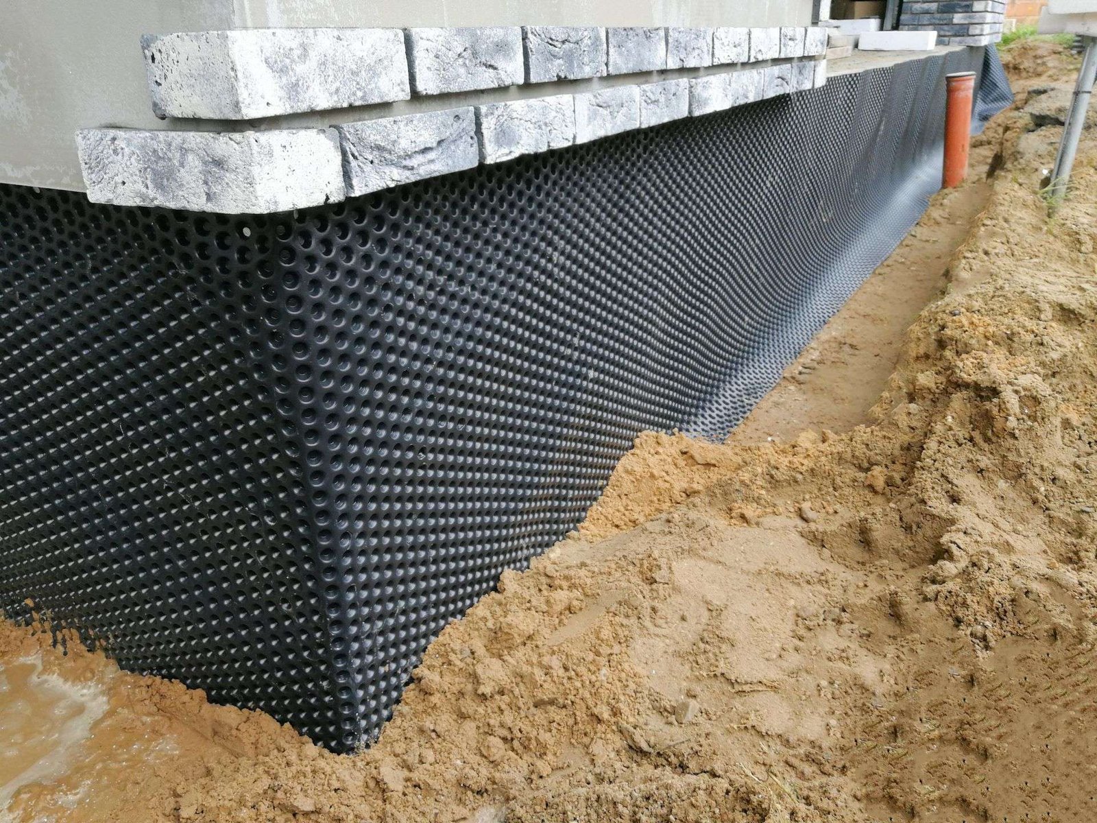 Exterior foundation wrapped in dimple board membrane with soil excavated away