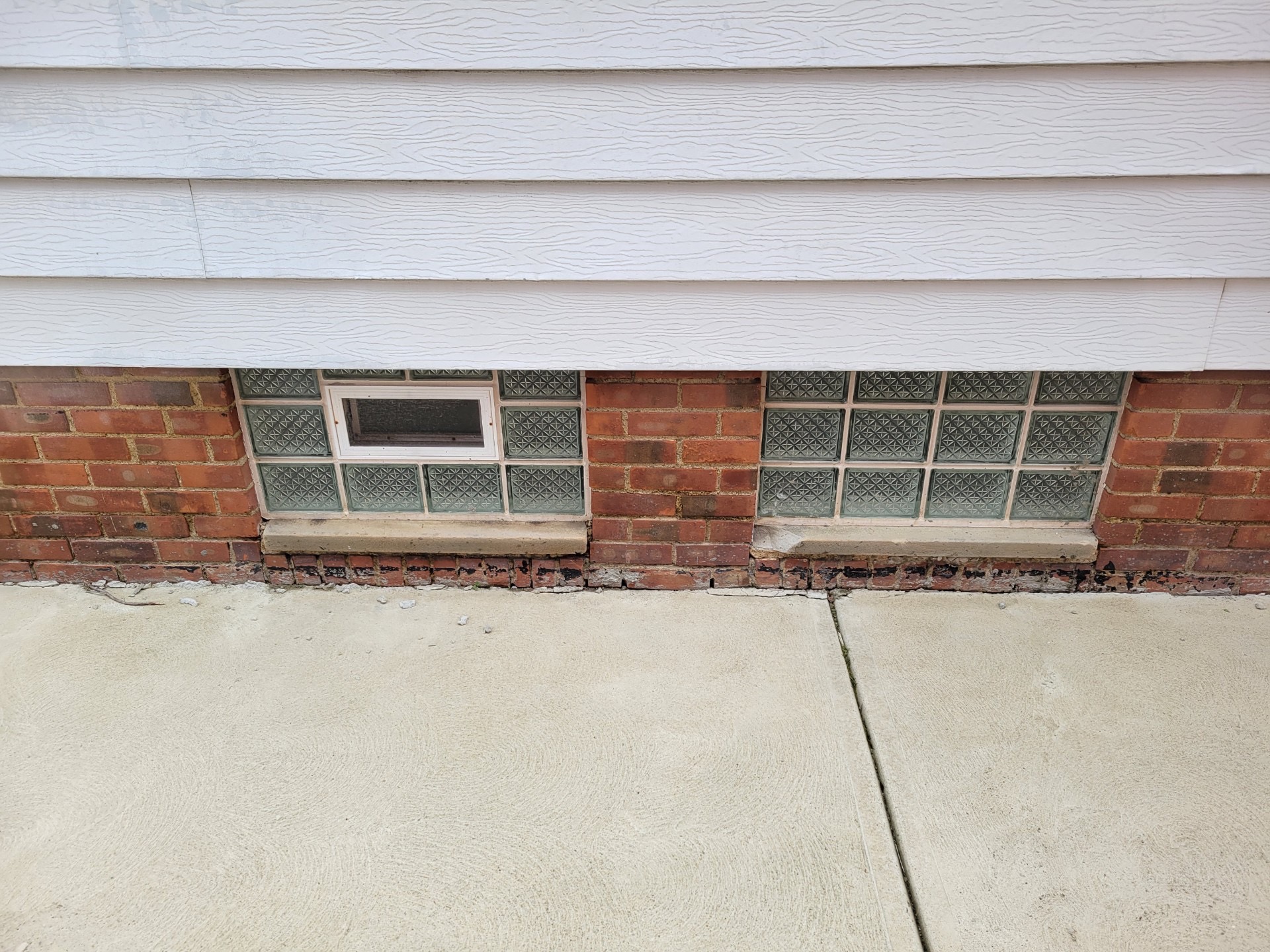 Old glass block basement windows with deteriorating brick foundation needing egress window replacement