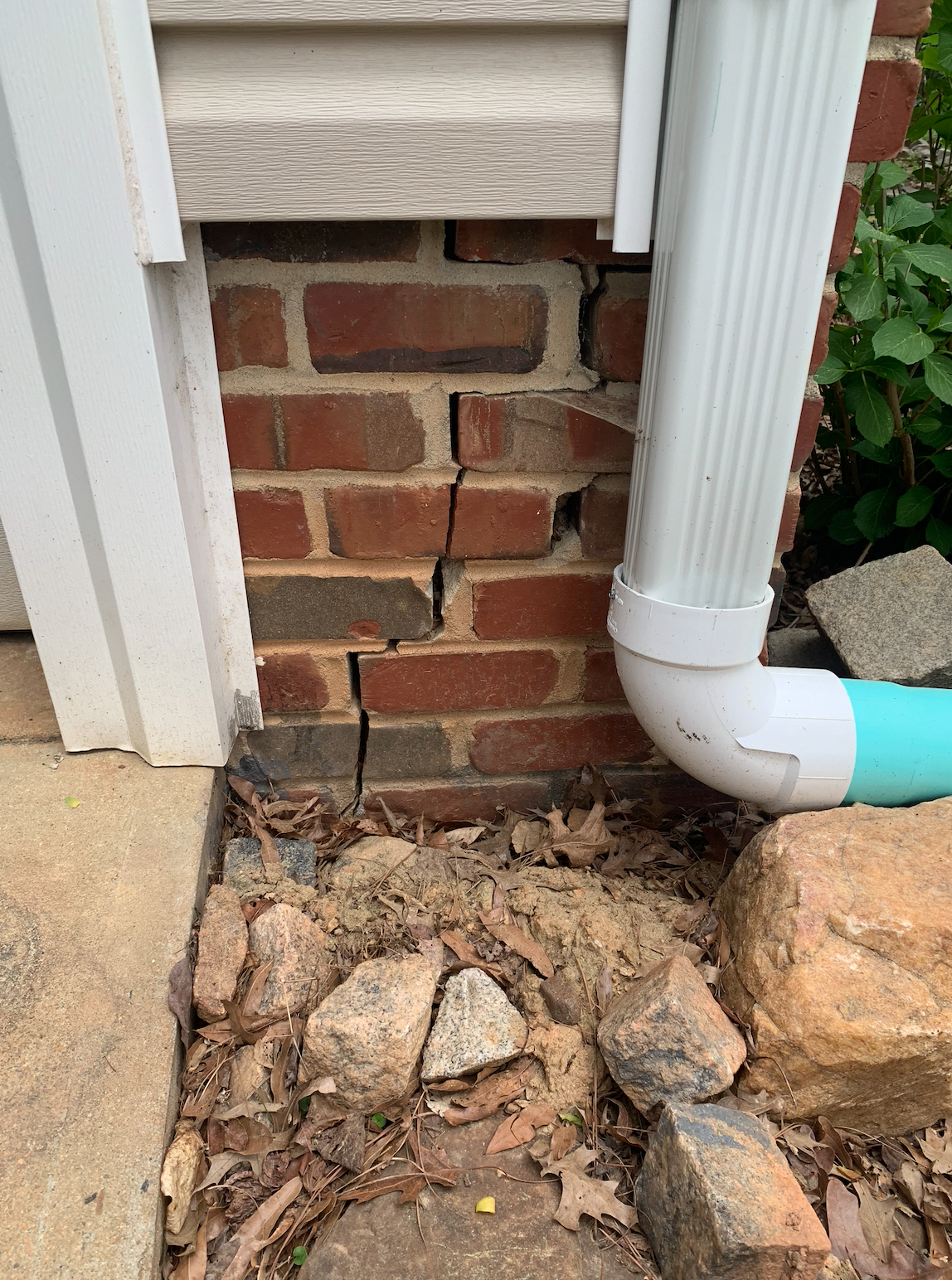 Cracked brick foundation wall near downspout