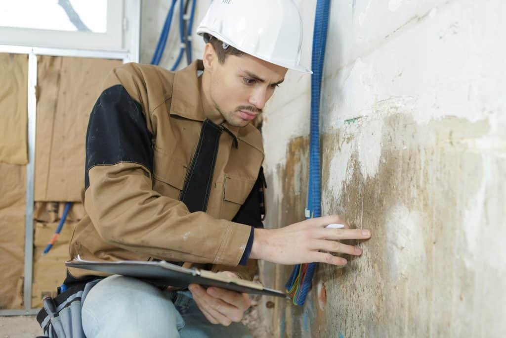 Technician inspecting a bowing basement wall for structural damage